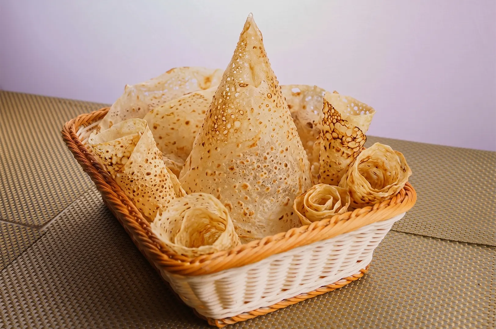Crispy Malaysian Roti Tissu served in a tall cone and rolls inside a woven basket.