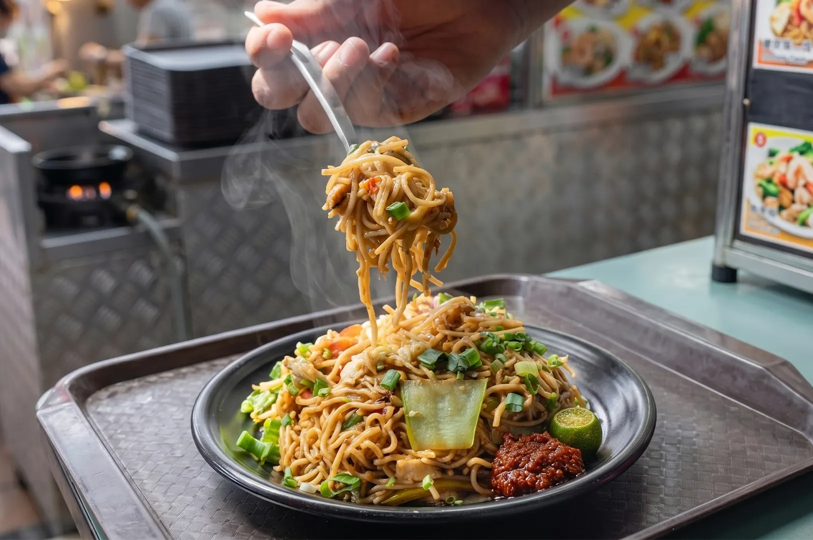 Steaming plate of Hokkien stir-fried noodles with scallions, sambal chili, and calamansi, served at an authentic street food stall.