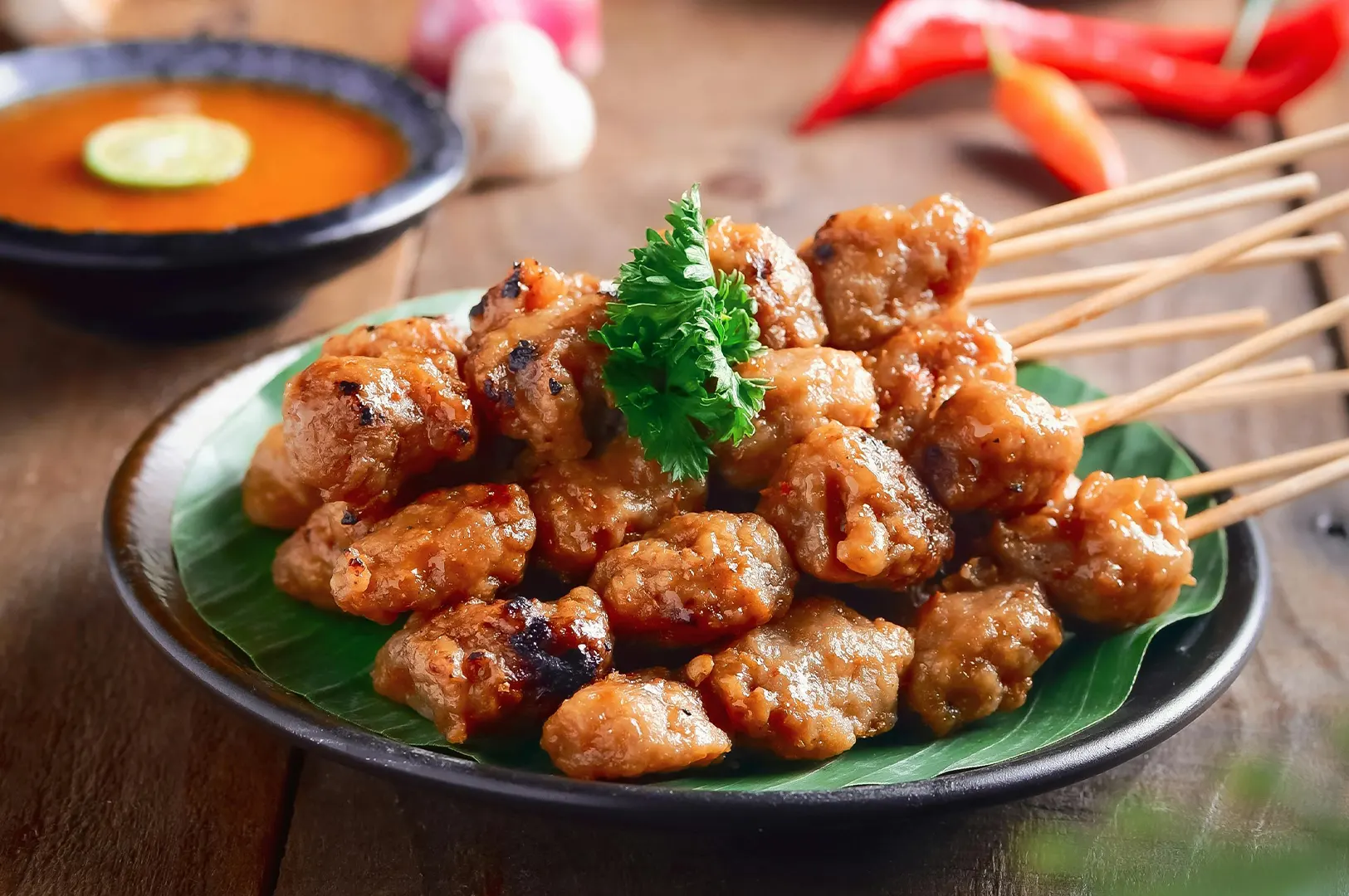 Grilled Indonesian chicken satay skewers served on banana leaves with a side of peanut sauce.