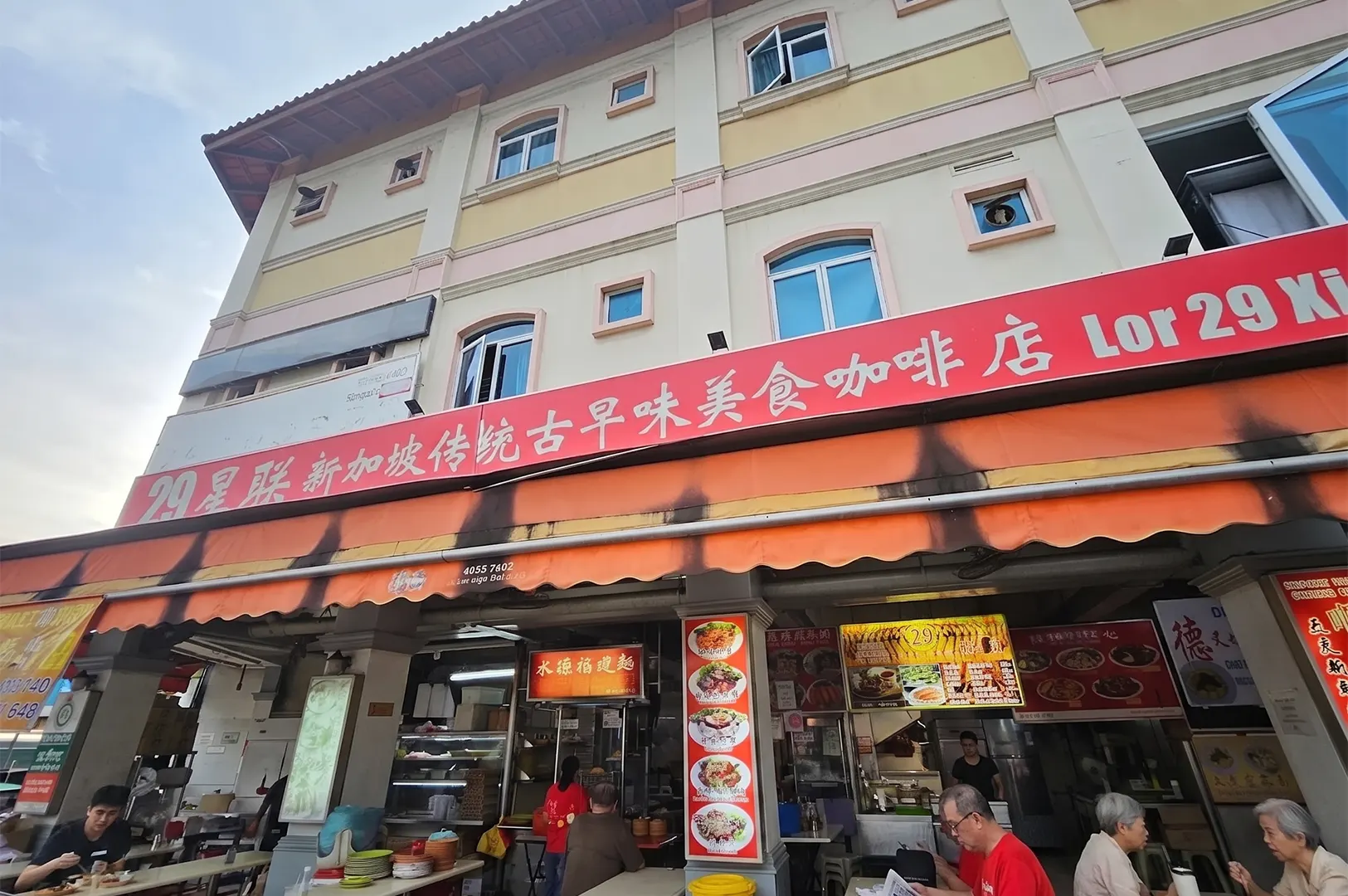 Exterior view of the Lor 29 Geylang Hokkien Mee coffee shop in Singapore, showing the red storefront sign and outdoor seating area.