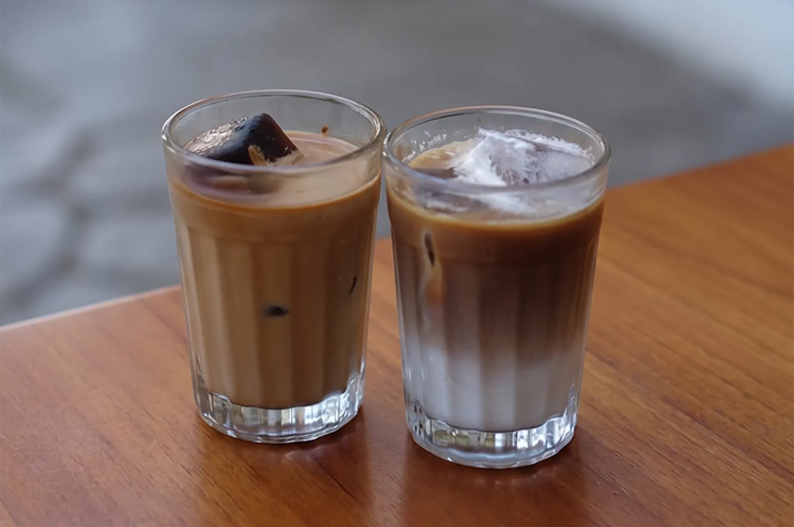 Two glasses of iced latte and iced coffee on a wooden table.